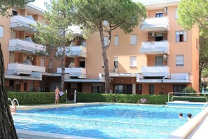 A swimming pool surrounded by apartment buildings with balconies, trees, and a hedge. - Bibione Apartment With Shared Pool (San Michele al Tagliamento)