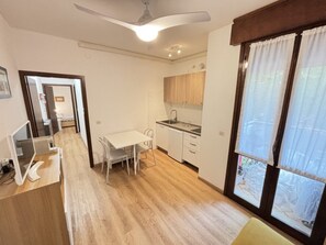 A compact kitchen with a dining area, a ceiling fan, and a large window with curtains. - Bibione Apartment With Shared Pool (San Michele al Tagliamento)