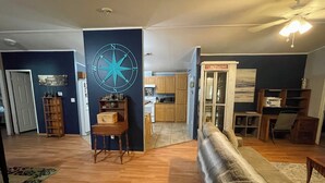 A living room with a large blue wall, wooden flooring, a sofa, a wooden chair, a small table, and a kitchen in the background. - Lazy Daze in Heart of Old Homosassa Custom Bar Great Outdoor Space Fire Pit (Homosassa)