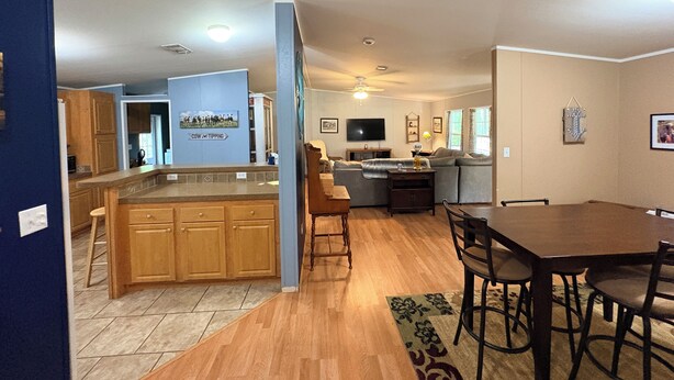 A spacious living area with a large dining table, a kitchen with wooden cabinets, and a ceiling fan. - Lazy Daze in Heart of Old Homosassa Custom Bar Great Outdoor Space Fire Pit (Homosassa)
