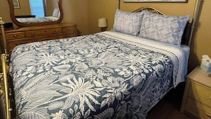 A bedroom with a bed, a dresser, a nightstand, a mirror, and a painting of the ocean. - Lazy Daze in Heart of Old Homosassa Custom Bar Great Outdoor Space Fire Pit (Homosassa)