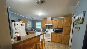 A kitchen with wooden cabinets, a white stove, a microwave, and a refrigerator. There are three stools at the counter. - Lazy Daze in Heart of Old Homosassa Custom Bar Great Outdoor Space Fire Pit (Homosassa)