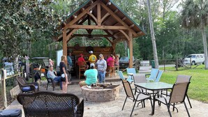 A covered outdoor seating area with tables and chairs, a barbecue grill, and a wooden structure with a pitched roof. - Lazy Daze in Heart of Old Homosassa Custom Bar Great Outdoor Space Fire Pit (Homosassa)