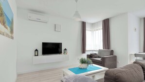 Ein modernes Wohnzimmer mit Flachbildfernseher, einer Wand-Klimaanlage, Deckenleuchte, Sofa, Couchtisch und einem fenster mit Vorhängen.