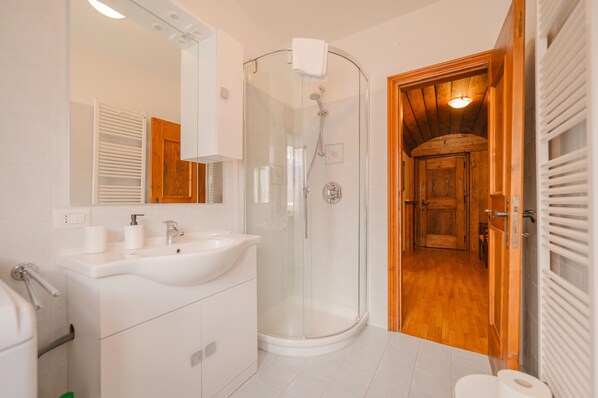 Un baño moderno con cabina de ducha de vidrio, lavamanos blanco y puerta de madera que da a otra habitación.