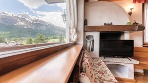 A cozy living area with a wooden bench, a flat-screen TV, and a fireplace. - Casa Verocai - Mountain View Terrace (Cortina d'Ampezzo)