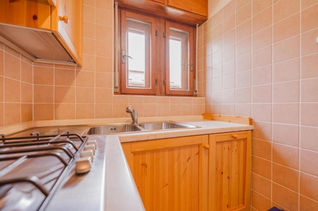A kitchen with a gas stove, a sink, wooden cabinets, and a window.