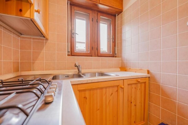 A kitchen with a gas stove, a sink, wooden cabinets, and a window. - Casa Verocai - Mountain View Terrace (Cortina d'Ampezzo)