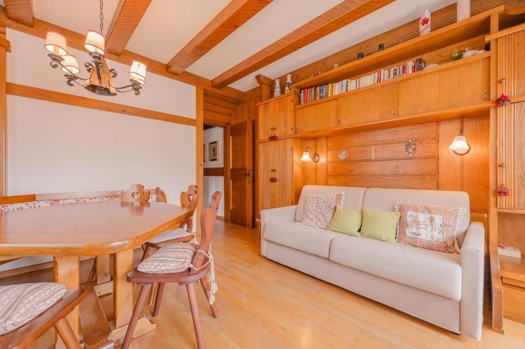 Ein Holzespeisesaal mit Stühlen, ein Sofa mit Kissen und ein Bücherregal mit Büchern.