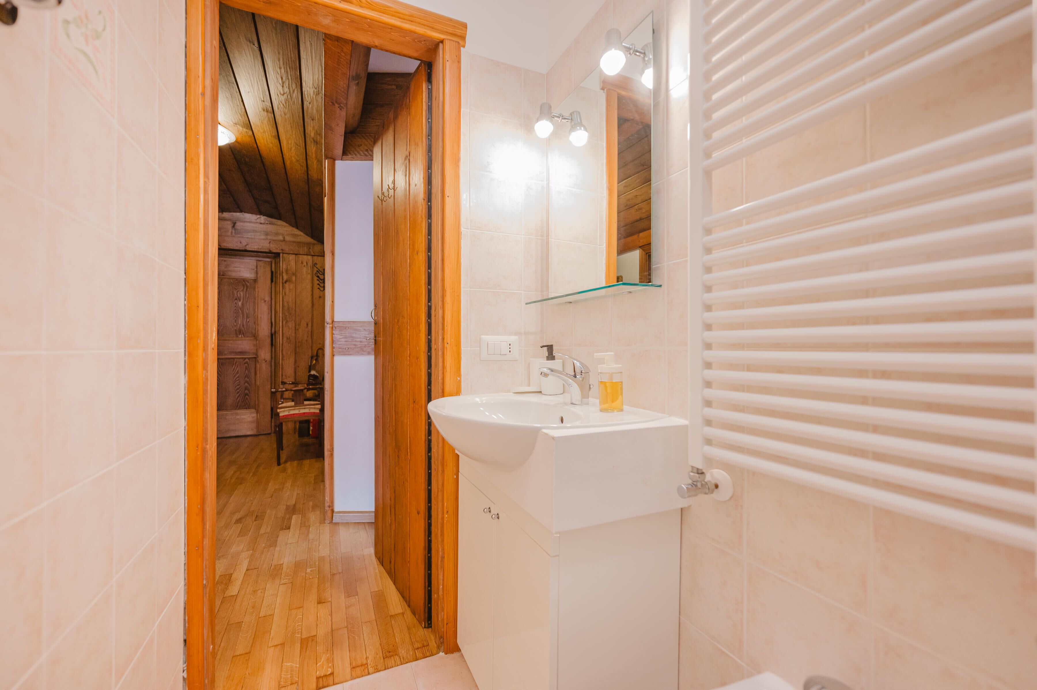 A bathroom with a wooden door, a white sink, a mirror, and a towel rack.