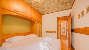 A hotel room with a large bed, wooden headboard, and a door leading to another room. - Casa Verocai - Mountain View Terrace (Cortina d'Ampezzo)