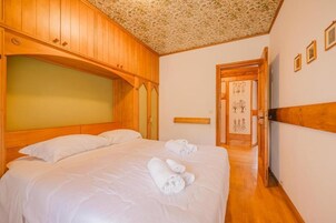 A hotel room with a large bed, wooden headboard, and a door leading to another room.