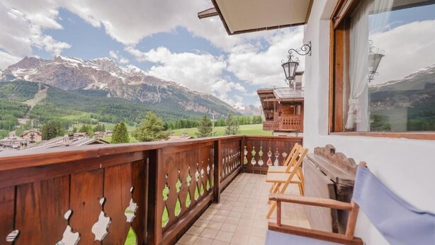 A balcony with a wooden railing, a view of mountains, and a wooden cabin structure. - Casa Verocai - Mountain View Terrace (Cortina d'Ampezzo)