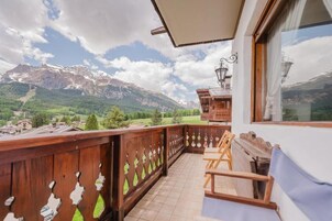 A balcony with a wooden railing, a view of mountains, and a wooden cabin structure.
