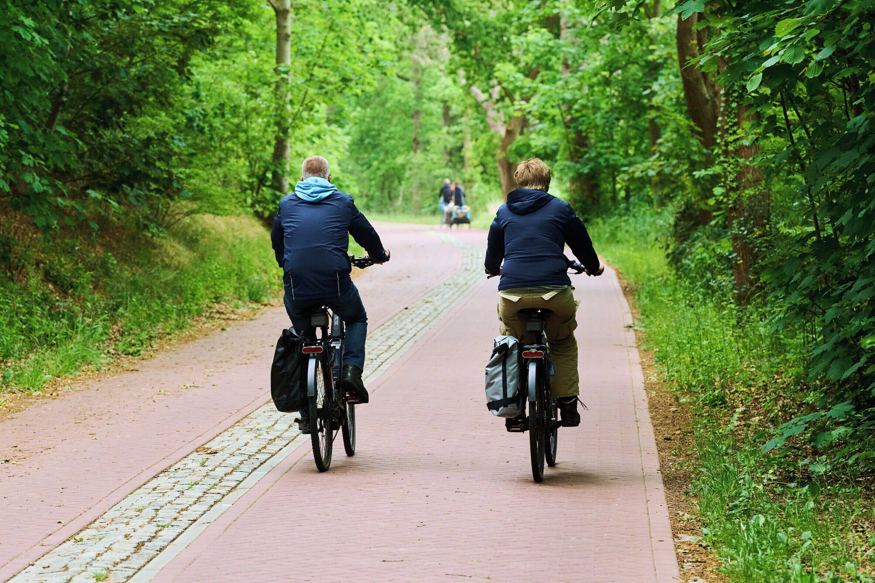 Deux cyclistes sur une piste cyclable asphaltée, entourés de verdure.