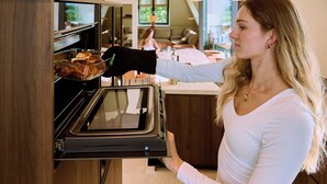 A woman opening a modern oven in a kitchen with wooden cabinets and a countertop. - Den Burg Holiday Home for 8 (Den Burg)