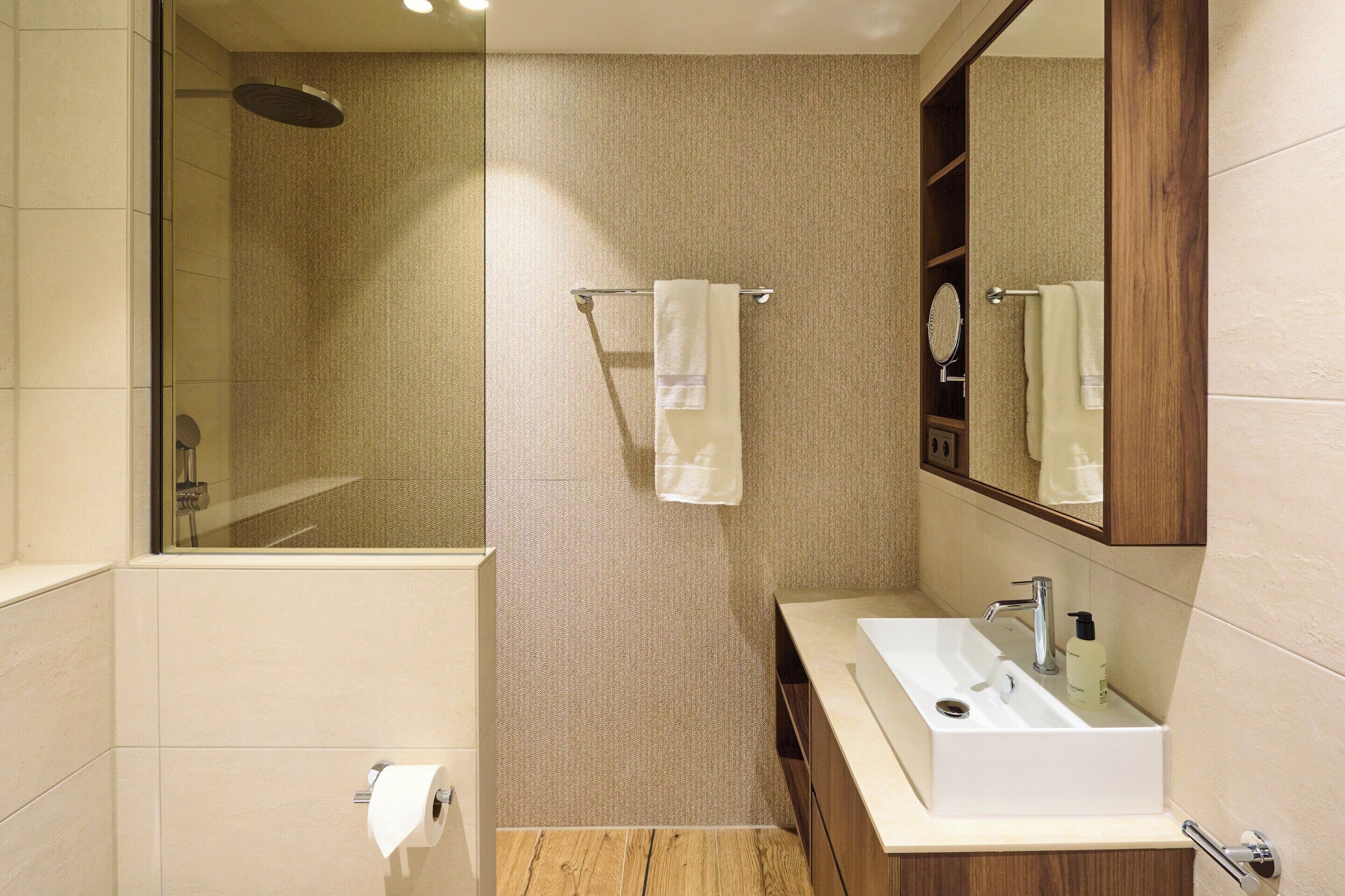 A bathroom with a shower, a sink, a mirror, and a towel rack.