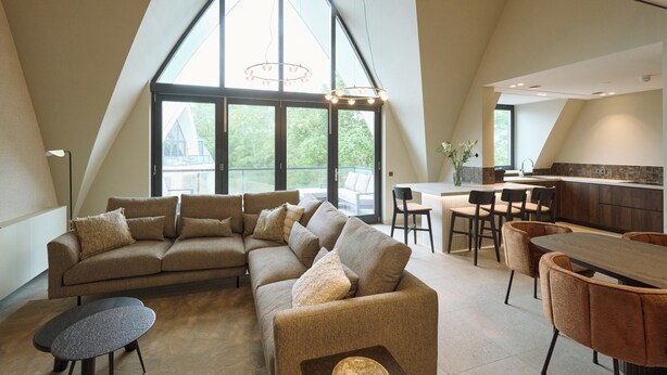 A modern interior with a large, sloped ceiling, a sectional sofa, a dining table with chairs, and a kitchen area. - Den Burg Holiday Home for 8 (Den Burg)