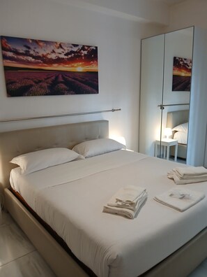 A neatly made bed with white linens and towels, a headboard, and a bedside table with a lamp.