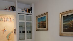 A dining area with a round table, white chairs, a white cabinet with glass doors, and two framed paintings on the wall. - Perry Guest House (Rome)