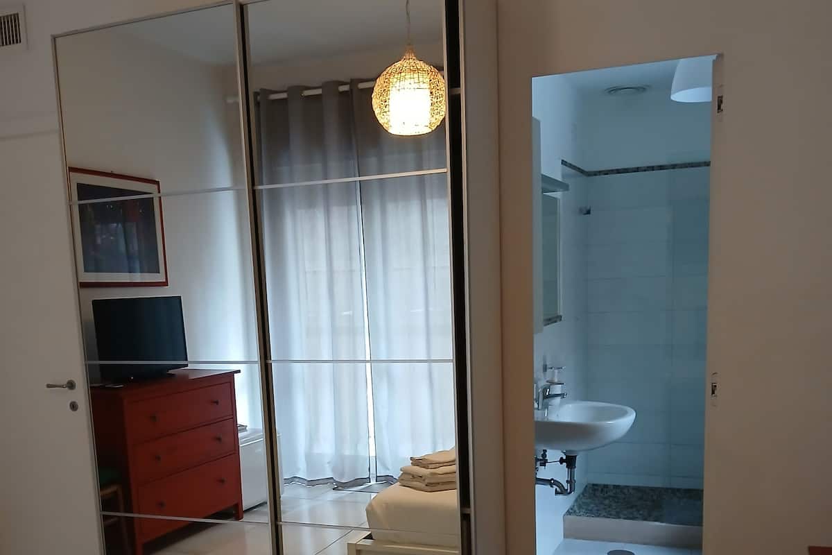 Een hotelkamer met een bed, een televisie, een rode dressoir, een spiegel en een badkamer met wastafel en douche.