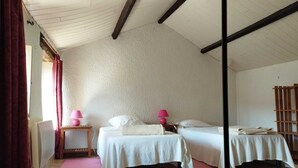 Una habitación con dos camas, techo de madera, alfombra rosa y una pequeña mesa de madera con lámparas.