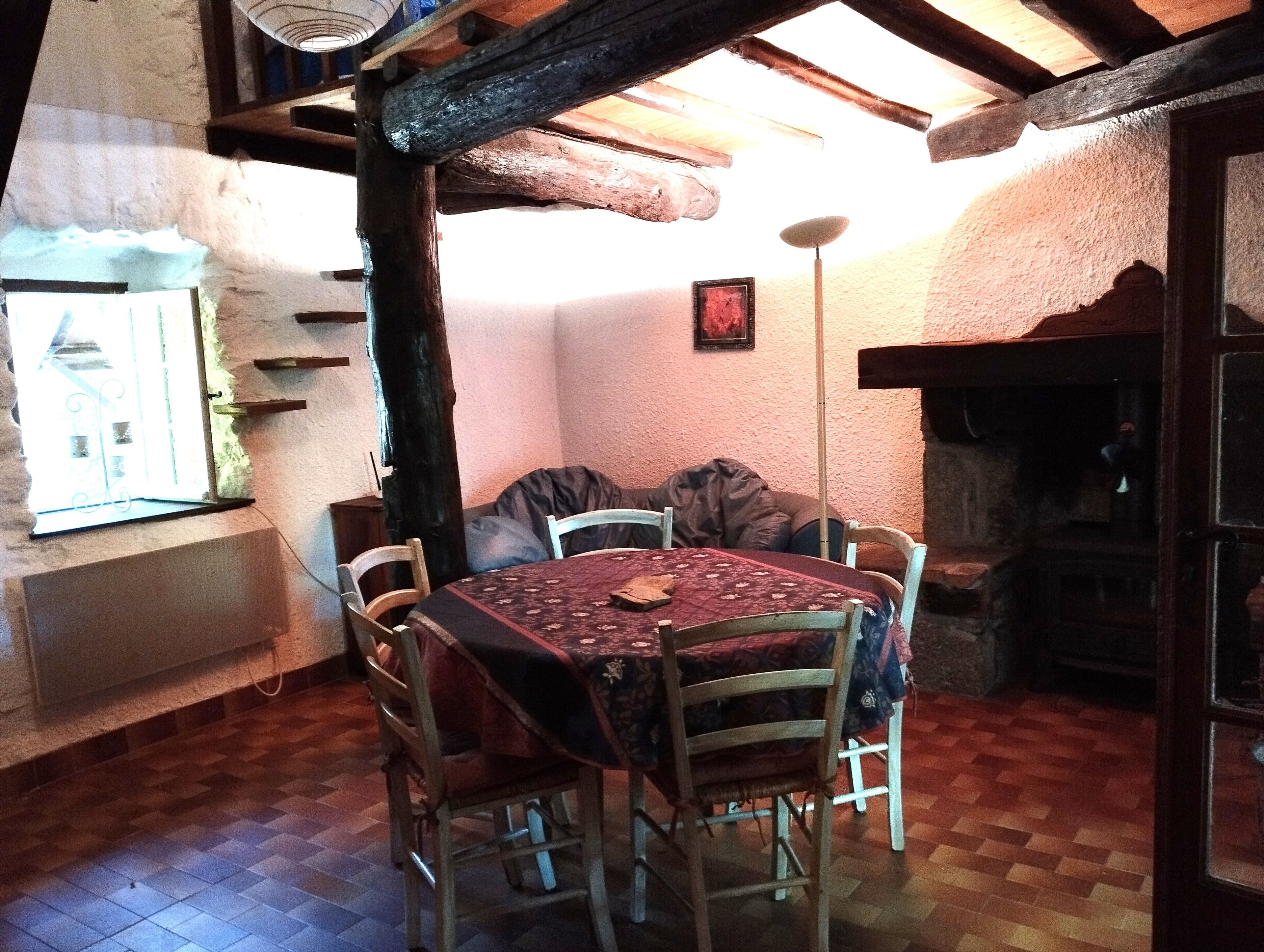 A rustic dining area with a wooden table and chairs, a thatched ceiling, and a stone wall.