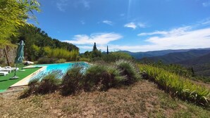Una piscina con vistas a colinas, rodeada de vegetación y un cielo despejado.