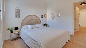 Un dormitorio con cama, mesitas de noche, una lámpara de pared y una puerta que da a otra habitación.