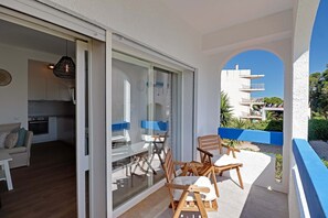 Un balcon avec des chaises et une table en bois, un coin cuisine avec des placards et une cuisinière, et une vue dégagée sur les bâtiments environnants.