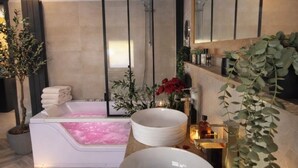 A modern bathroom with a bathtub, two sinks, a large mirror, and decorative plants. - Leonard's (Bièvres)