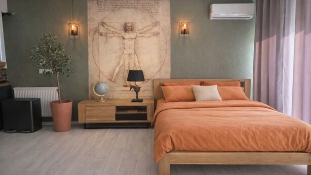 A bedroom with a wooden bed, a nightstand with a lamp, a wall-mounted air conditioner, and a large tapestry. - Leonard's (Bièvres)