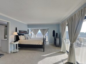 Ein Schlafzimmer mit Bett, Nachttischen, einem Fernseher und Balkonblick.