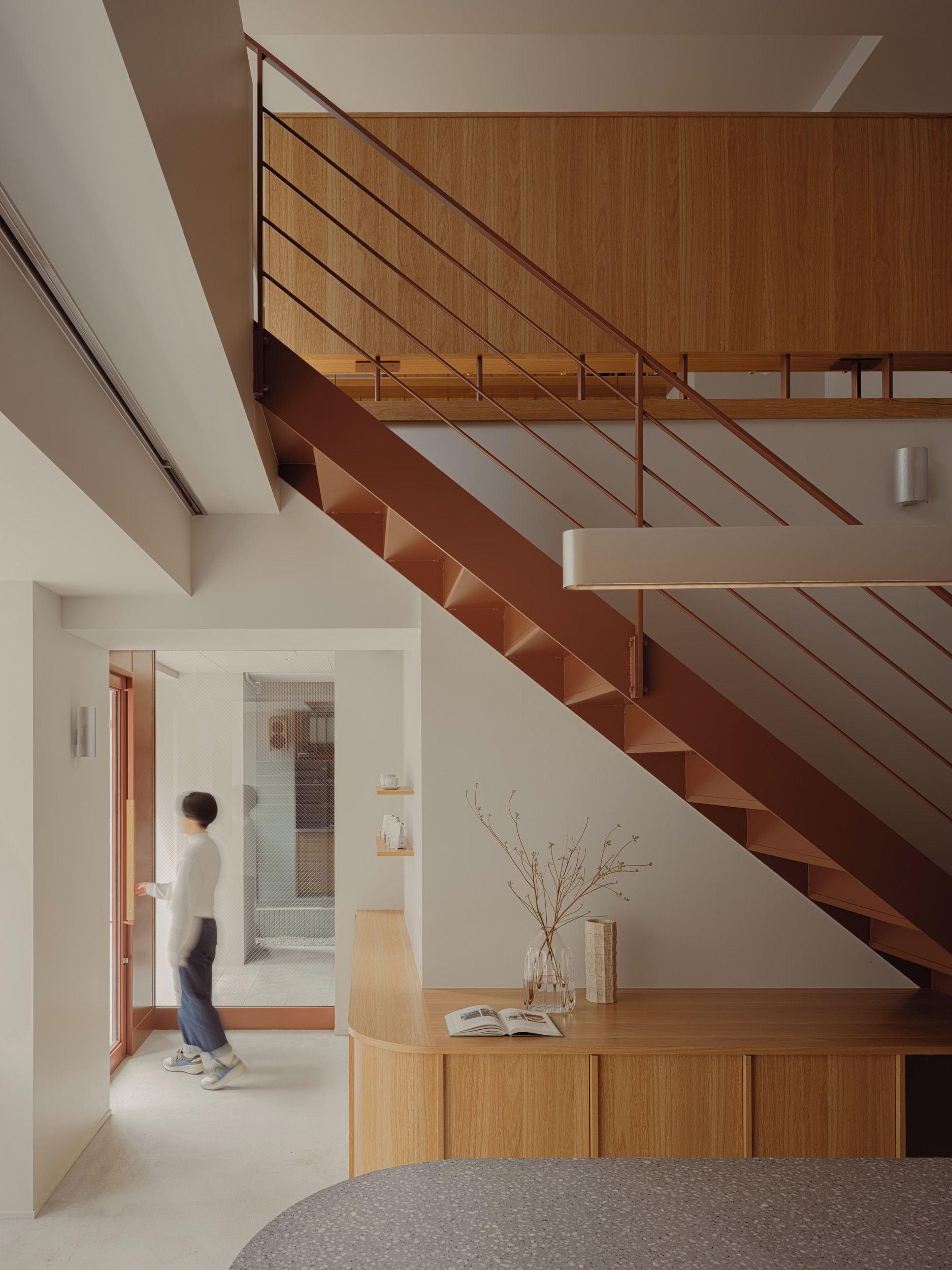 A modern interior with a wooden staircase, a glass door, and a round table with a vase.