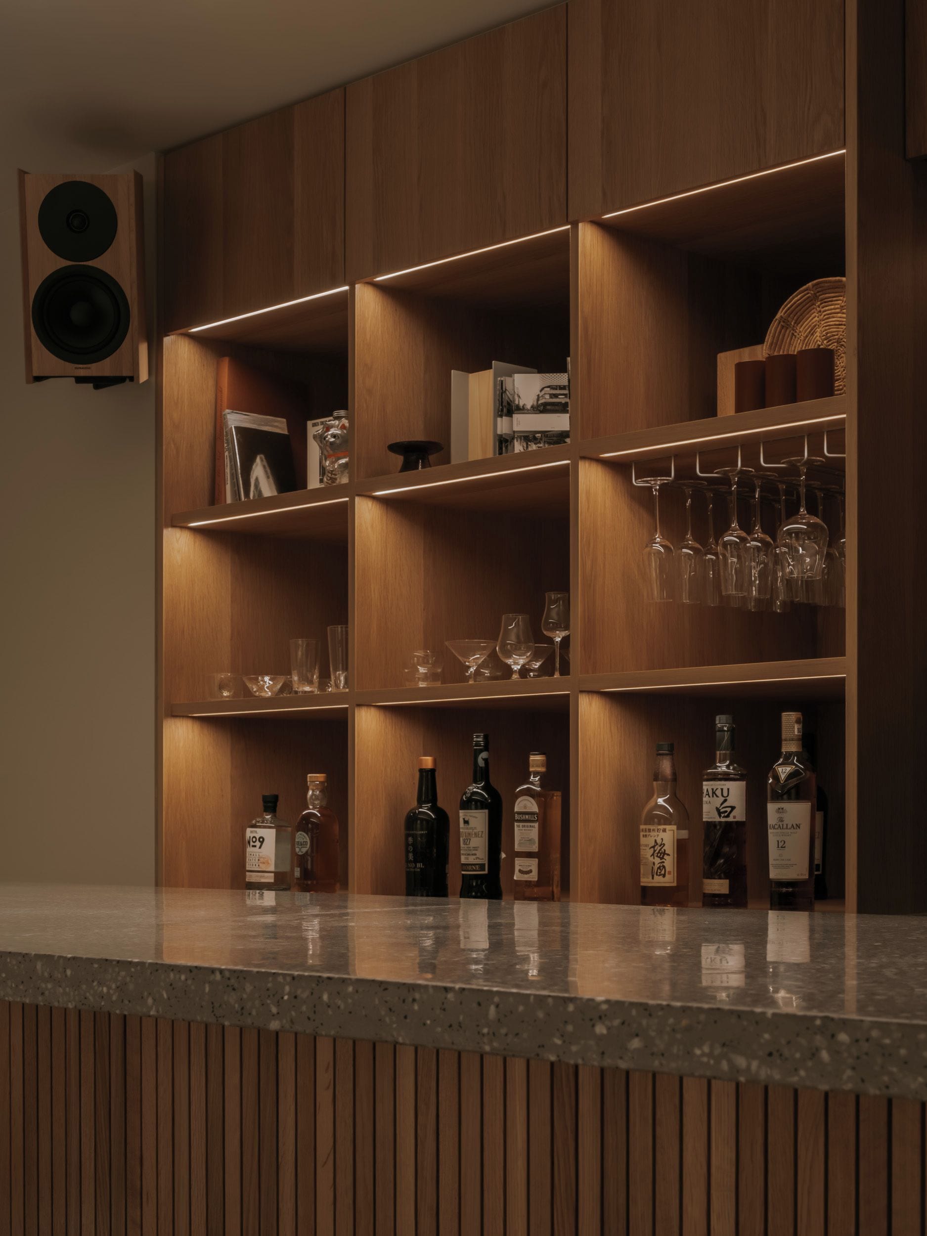 Una zona de bar con estanterías de madera, copas de vino y botellas de licores.