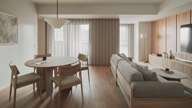 Ein modernes Wohnzimmer mit einem runden Esstisch, Holzsesseln, einer Couch, einem Fernseher und einem großen Fenster mit Vorhängen.