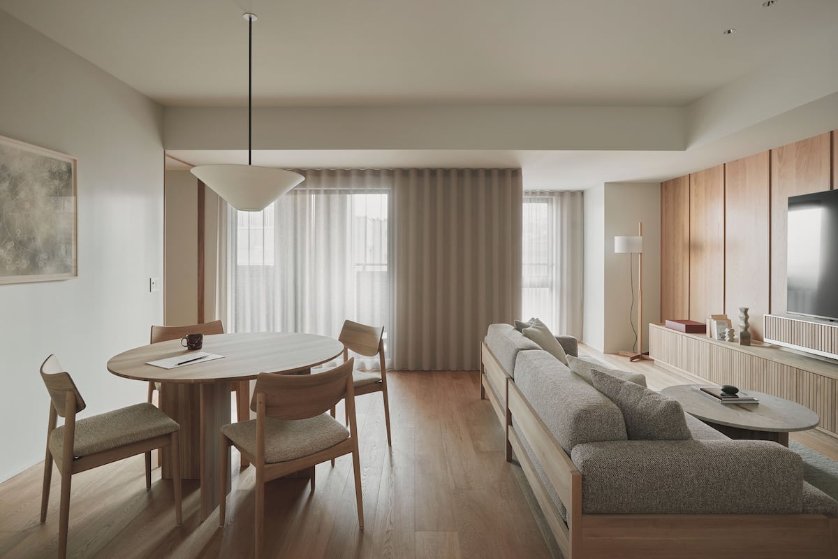 A modern living room with a round dining table, wooden chairs, a sofa, a TV, and a large window with curtains.