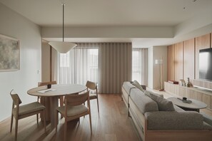 A modern living room with a round dining table, wooden chairs, a sofa, a TV, and a large window with curtains. - TOMI. Ginza (Tokyo)