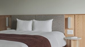 Ein modernes Hotelzimmer mit einem großen Bett, einem Holzkopfteil, Nachttischen und einer Wandleuchte.