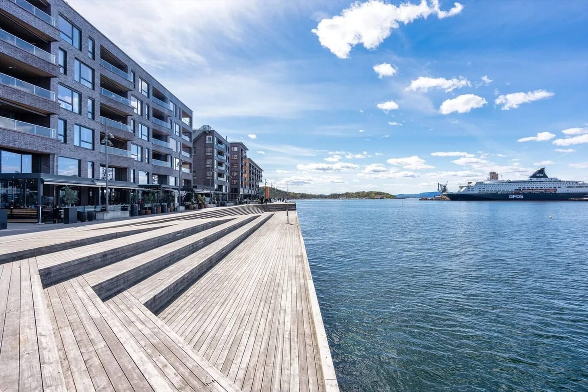 Eine Uferpromenade mit einem modernen Gebäude, einem Kreuzfahrtschiff und blauem Himmel.