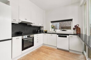 A modern kitchen with white cabinets, a black countertop, and a window with a view of a brick wall.