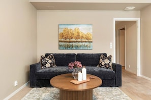 A living room with a dark blue sofa, a round wooden coffee table, and a painting of trees on the wall. - Urban Escape - Only Steps From the Waterfront (Oslo)