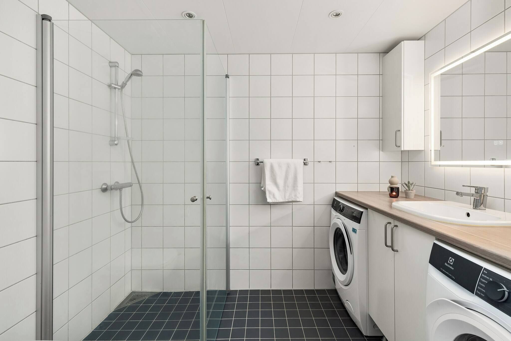 Ett modernt badrum med en dusch som är avskärmad med glasväggar, en tvättmaskin, ett handfat och en spegel.