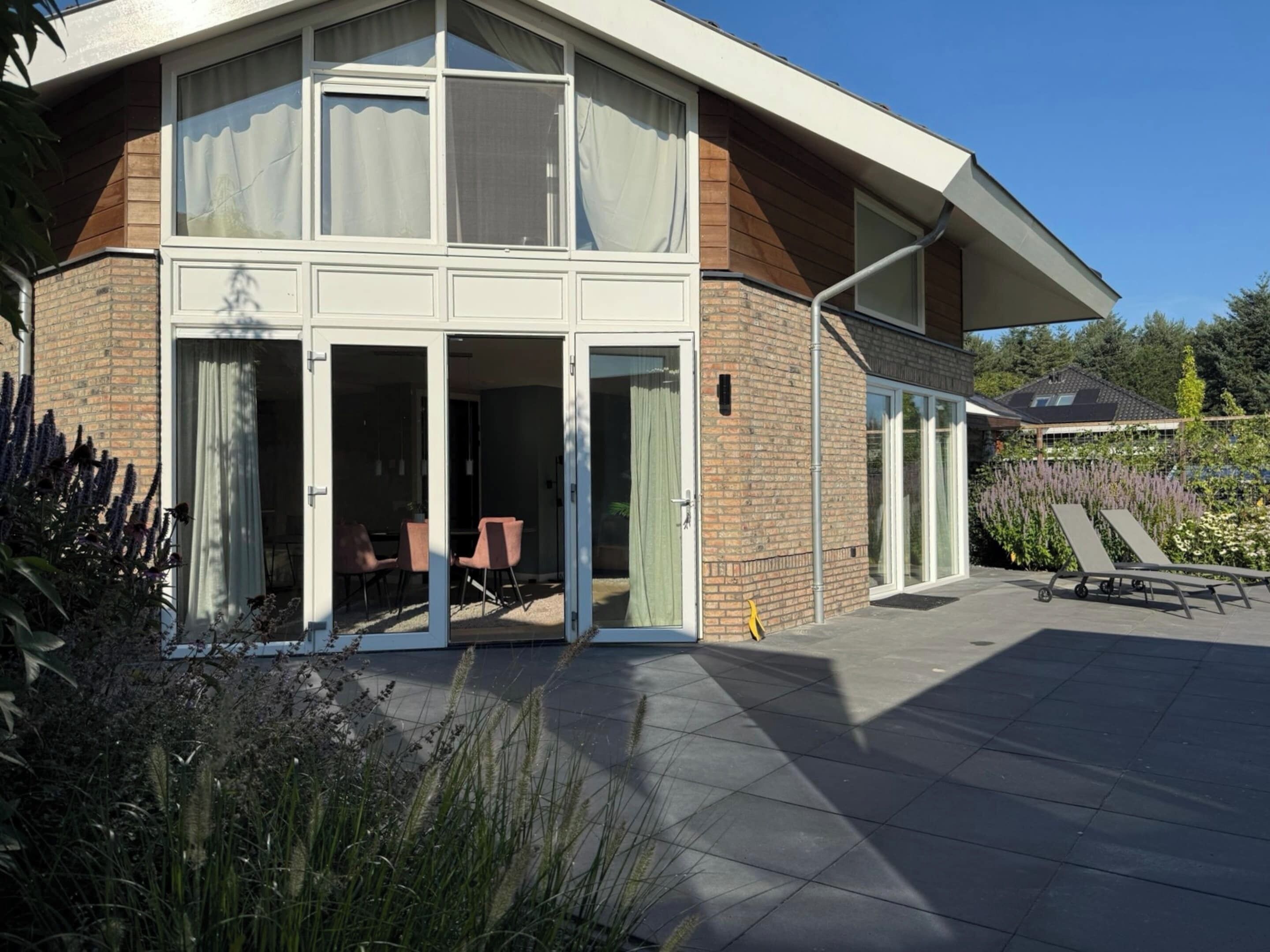 Une maison moderne dotée d’un patio, de grandes fenêtres et d’un espace extérieur aménagé et couvert.