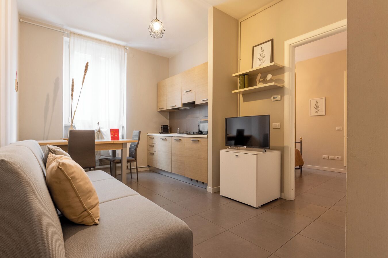 Un salon moderne comprenant un canapé, une table à manger avec des chaises, un coin cuisine et un téléviseur posé sur un meuble.