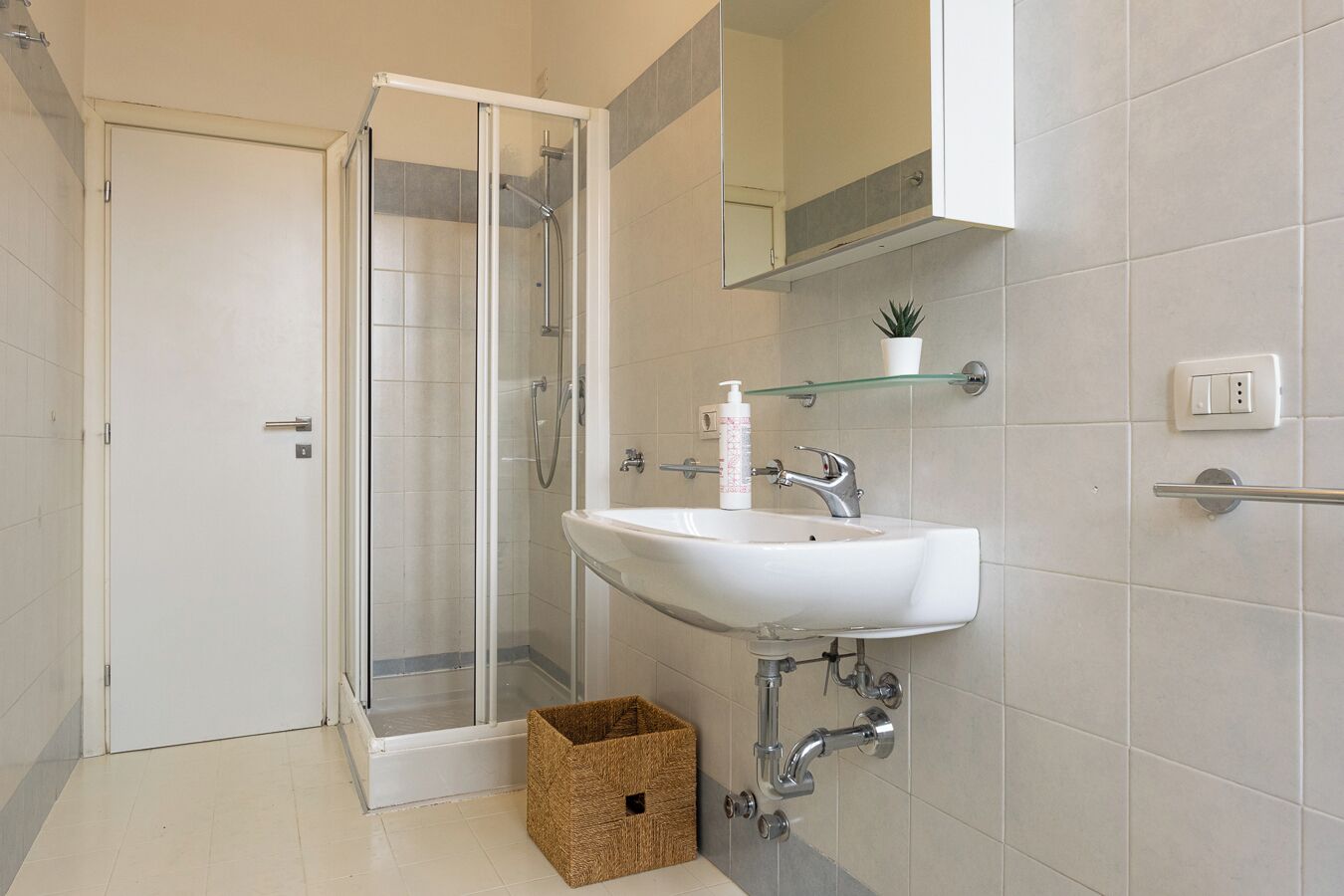 A bathroom with a glass shower enclosure, a white sink, and a mirror above it.