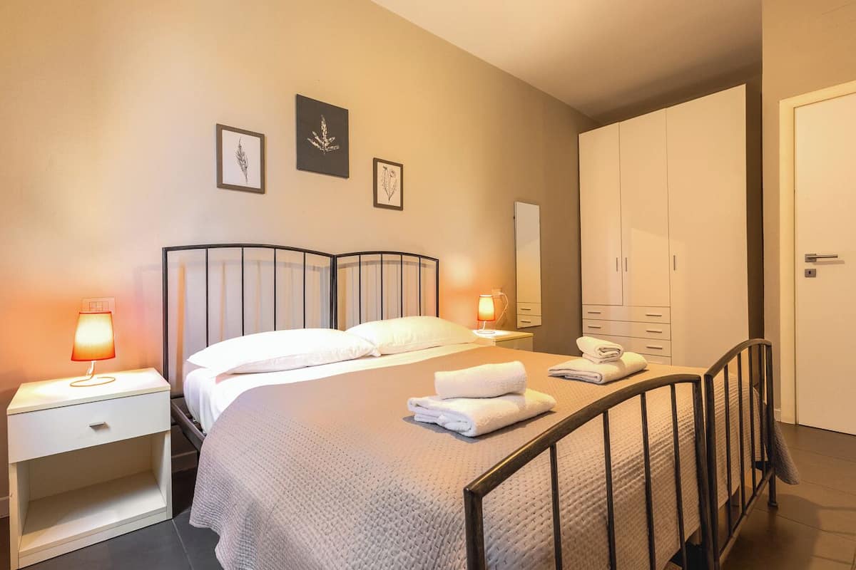 Una habitación de hotel con cama, mesitas de noche, armario e impresiones botánicas enmarcadas en la pared.