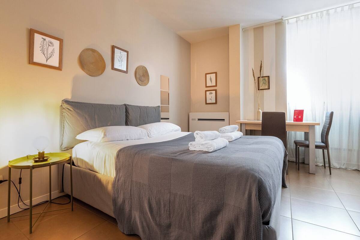 Habitación de hotel con cama, mesita de noche, silla, escritorio y ventana con cortinas.