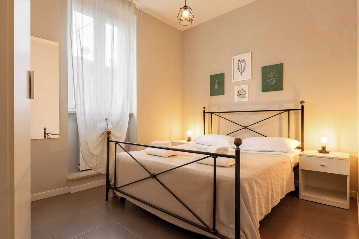 Un dormitorio con cama, mesitas de noche, ventana con cortinas y decoración en la pared.