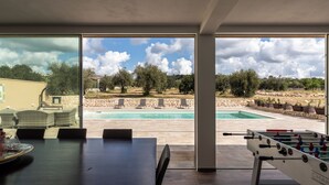 Un espacio interior moderno con vista a la piscina, una mesa de fútbol y un comedor.